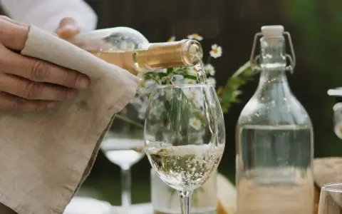 En hand häller upp vitt vin i ett glas. Den perfekta vitt vin temperatur är avgörande för smaken.