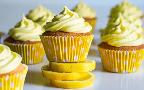 Gula citronmuffins med fluffig frosting, serverade i prickiga formar. Perfekt för ett citronmuffins recept!
