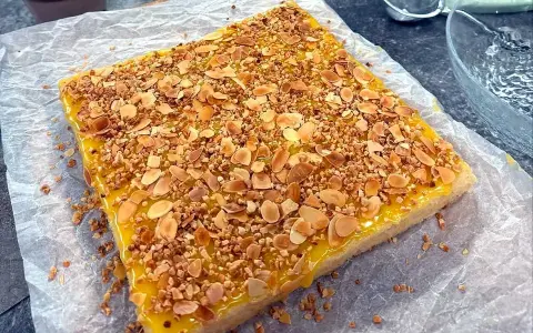En fyrkantig silviakaka med gul glasyr och strössel av hackade nötter och mandel. Perfekt för ett fika-recept!