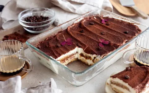 En krämig tiramisu i glasform, perfekt för ett enkelt tiramisu recept. Toppad med kakao, kaffebönor och lila blommor.