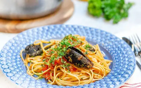 En tallrik med frutti di mare pasta, toppad med färsk persilja och serverad i en blåmönstrad skål.