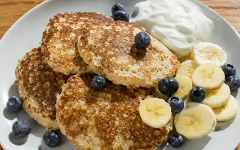 En tallrik med bananpannkakor, blåbär, bananskivor och en klick yoghurt. Ett enkelt bananpannkaka recept för en god frukost.