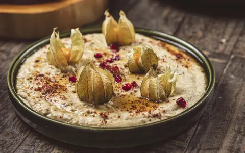 Krämig baba ganoush toppad med physalis och granatäppelkärnor på en rustik träyta.
