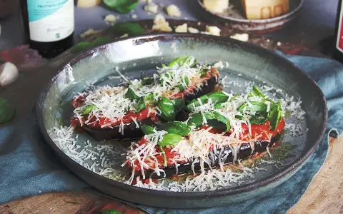 Halverade auberginer toppade med tomatsås, basilika och riven ost, redo att tillagas i ugnen. En härlig aubergine i ugn.