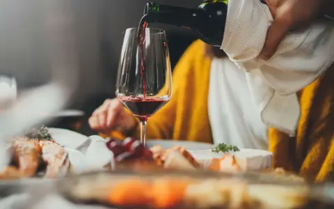 Rödvinet hälls upp i ett glas vid en middagsbjudning. En person i gul tröja sitter bakom. Frågan om hur mycket vin per person är relevant för en trevlig kväll.