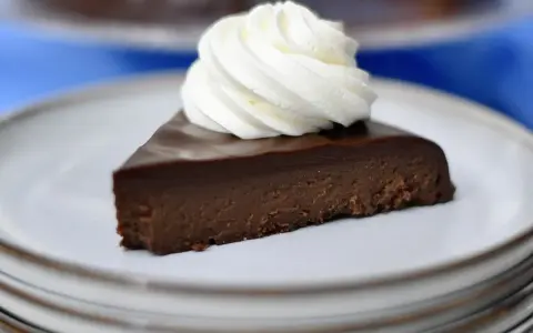 En bit krämig fransk chokladtårta med en virvel av vispad grädde på en ljusgrå tallrik.
