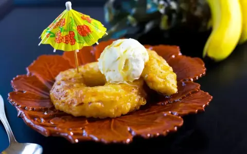 Friterad banan med vaniljglass och en liten gul parasoll. En tropisk dessert som smakar sommar.
