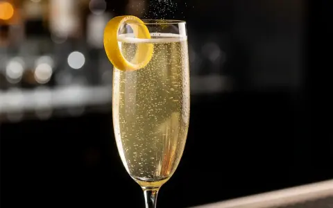 Ett glas French 75 med bubblor och citronskal. En klassisk drink med en intressant french 75 historia.