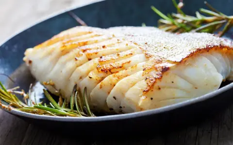 En saftig bit fryst torsk i ugn, gyllene och perfekt tillagad, med rosmarin i en mörk panna.
