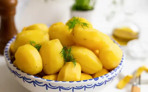 Nyskållade, gula potatisar i en blåvit skål, redo att koka. Dillkvistar ger en fräsch touch.