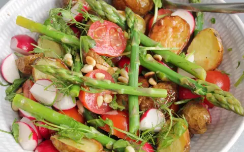 En härlig rostad potatissallad med sparris, rädisor och körsbärstomater, toppad med pinjenötter och dill.