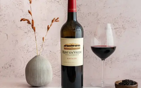 En flaska Rust en Vrede Estate vin, perfekt till oxfilé, står bredvid ett glas rött vin och en liten skål med pepparkorn.