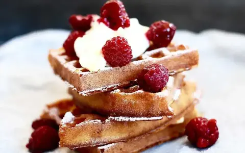En stapel gyllene belgiska våfflor toppade med vispgrädde och färska hallon, pudrade med florsocker. En härlig frukost eller efterrätt.