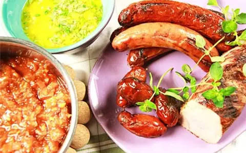 Grillad fläskfilé och korvar med en härlig bbq sås. Bredvid står en skål med en tomatröra och en grön sås.