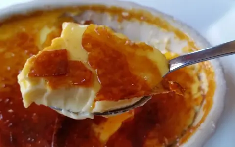 En sked tar en bit av en krämig creme brulee med karamelliserat sockerlock.
