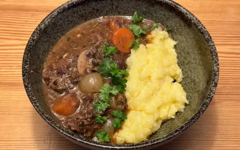En skål med mustig biff bourguignon med möra köttbitar, champinjoner, lök och morötter, serverad med krämigt potatismos och garnerad med persilja.
