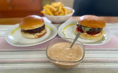 Två hamburgare med pommes frites och en skål med hemlagad hamburgerdressing. Perfekt för en mysig hemmakväll!
