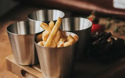 Friterade pommes i kastrull, serverade i små metallmuggar. En läcker aptitretare som påminner om hemgjord snabbmat.