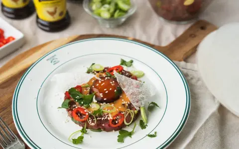 En läcker asiatisk råbiff med chili, salladslök och sesamfrön, serverad på en vit tallrik med gröna kanter.