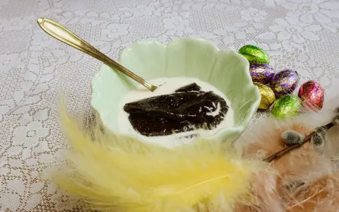 En skål med memma och grädde, redo att avnjutas. Ett gyllene påskägg och fjädrar fulländar bilden av ett klassiskt memma recept.