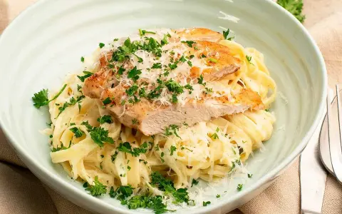 En krämig portion chicken alfredo med tagliatelle, toppad med grillad kyckling, parmesan och färsk persilja.