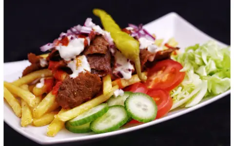 En tallrik med kebab, pommes frites, tomater, gurka, sallad och en grön chili. Perfekt för att inspireras till ett gott kebabsås recept.