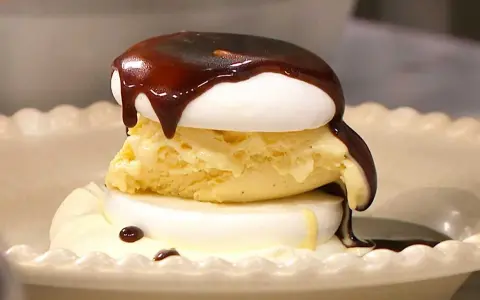 En läcker banana split med vaniljglass, maräng och chokladsås som rinner ner.