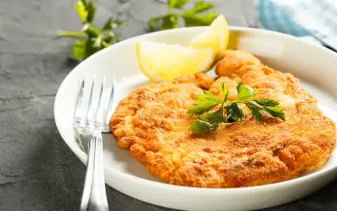 En gyllene schnitzel med citronklyfta och persilja, redo att avnjutas med ett glas vin till schnitzel.