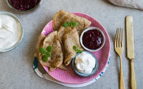 En tallrik med glutenfria pannkakor, serverade med sylt och grädde. En härlig frukost eller fika!
