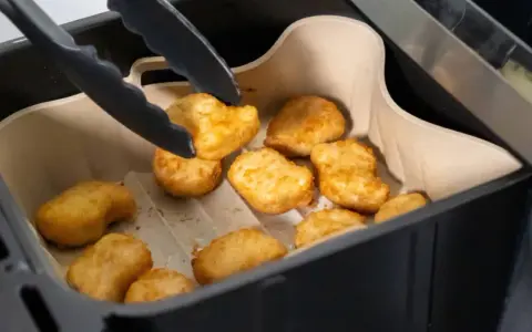 Tång tar upp gyllene, krispiga tater tots ur en airfryer.