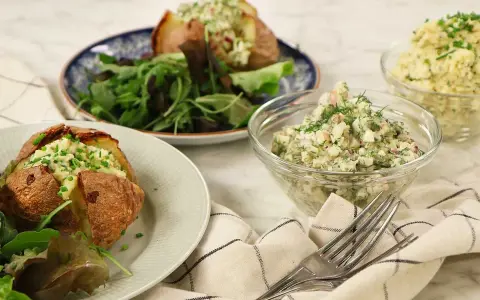 Två bakade potatisar med en krämig bakad potatis fyllning, serverade med en fräsch sallad och två skålar med olika röror.