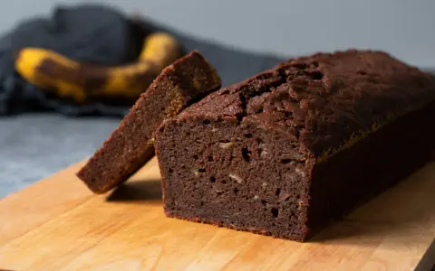 Chokladig banankaka, perfekt för ett enkelt banankaka recept. En skiva är uppskuren och en övermogen banan ligger i bakgrunden.
