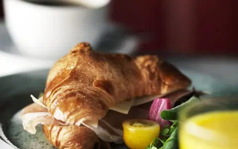 En gyllene croissant fylld med skinka och ost, serverad med grönsaker och juice. Perfekt för en snabb frukost eller lunch, som ett enkelt croissant recept.