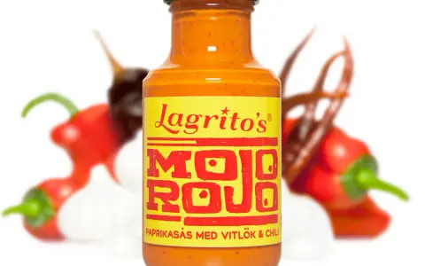En flaska Lagrito's Mojo Rojo, en paprikasås med vitlök och chili, omgiven av färska chilis och vitlök.