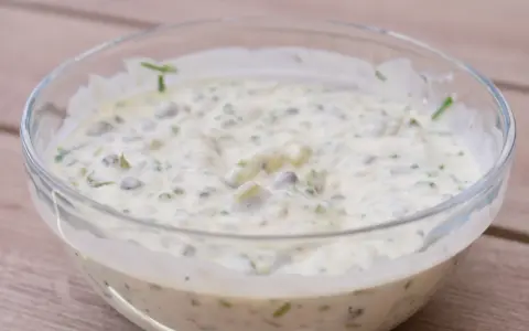 En krämig kall sås till fisk, med kapris och örter, serverad i en glasskål på en träyta.