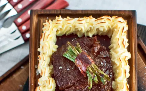 En saftig biff med gröna bönor inslagna i bacon, omgiven av krispig potatispuré. Ett perfekt plankstek recept för en festmåltid.