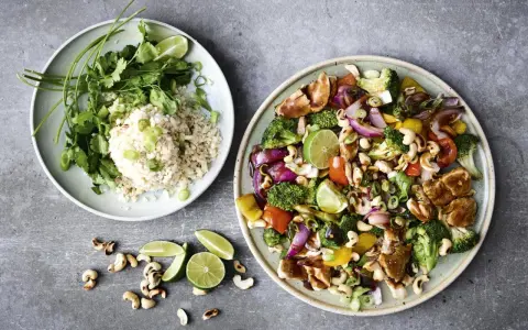 Två tallrikar med mat. En med ris, koriander och salladslök. Den andra med kyckling, broccoli, paprika, cashewnötter och lime. Perfekt för nyttiga recept.