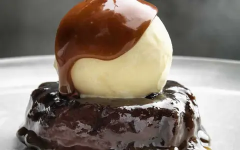 En läcker sticky toffee pudding med en kula vaniljglass och varm kolasås som rinner över.