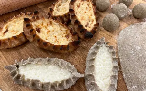 Färdiga piroger och ingredienser för piroger recept. Degbollar, kavlad deg och nybakade piroger med ostfyllning.