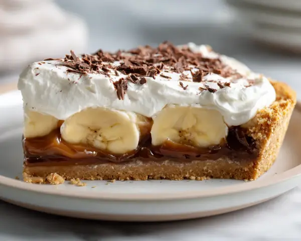 En bit krämig banoffee paj med banan, kolasås, vispgrädde och chokladströssel.