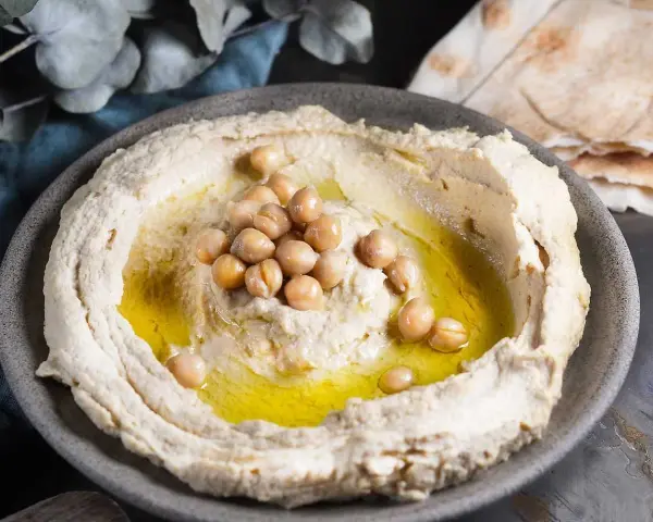 Krämig hummus med kikärtor och olivolja, perfekt för ett enkelt hummus recept. Serveras med pitabröd.