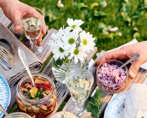 En härlig sommarmåltid med inlagd sill, hackad rödlök och vitt vin till sillen. Blommor och grönska i bakgrunden.