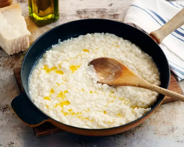 Krämig risotto i panna, med parmesan, olivolja och en träsked. Perfekt för ett enkelt risotto recept.