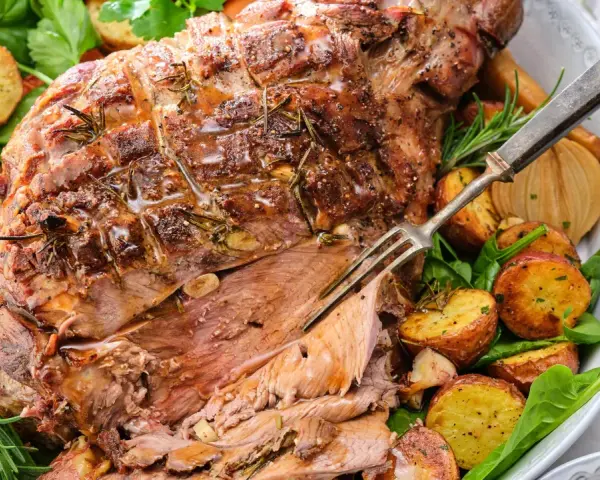 En saftig lammstek med ben, omgiven av rostade potatisar, lök och färska örter. Perfekt för en festlig middag.