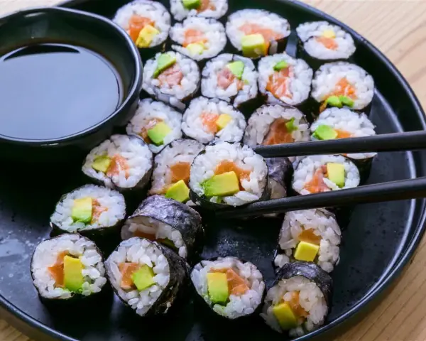 En tallrik med hemgjord sushi, perfekt för ett enkelt sushi recept. Lax och avokado rullade i ris och nori, med en skål sojasås.