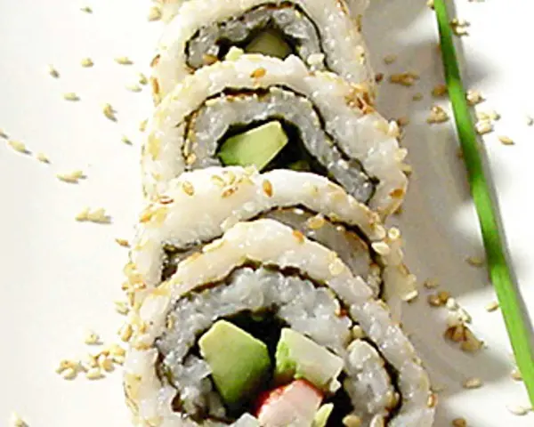 En närbild på en california roll med sesamfrön och en grön garnityr.