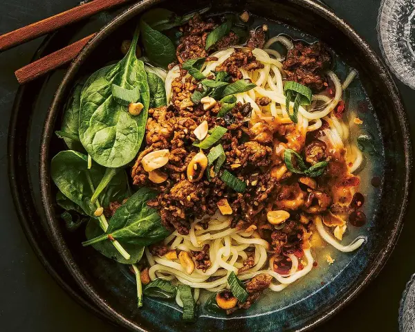 En skål med dan dan nudlar, toppad med köttfärs, jordnötter och sallad.
