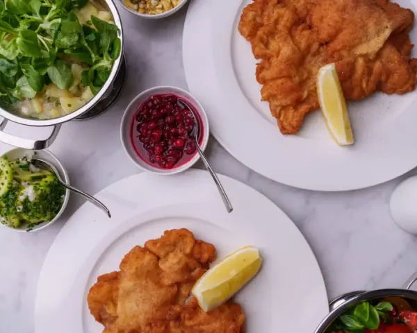 Två krispiga schnitzlar med citronklyfta, serverade med potatissallad, lingon, gurksallad och en krämig sås. Ett perfekt schnitzel recept för en festmåltid.