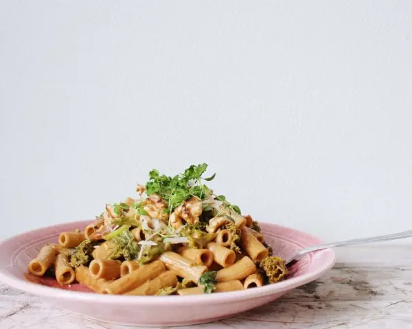 En läcker vegetarisk pasta med broccoli, valnötter och färska örter på en rosa tallrik.