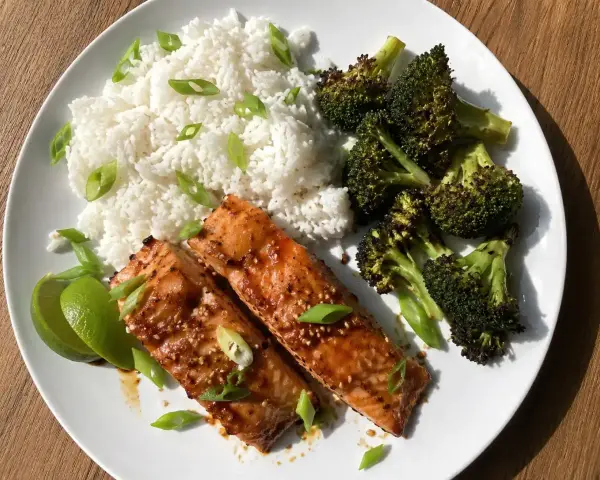 Två saftiga filéer av asiatisk lax serveras med fluffigt ris, rostad broccoli och limeklyftor.